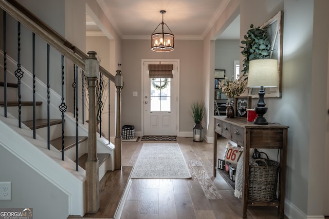 foyer entrance featuring hardwood / wood-style flooring, ornamental molding, and a chandelier