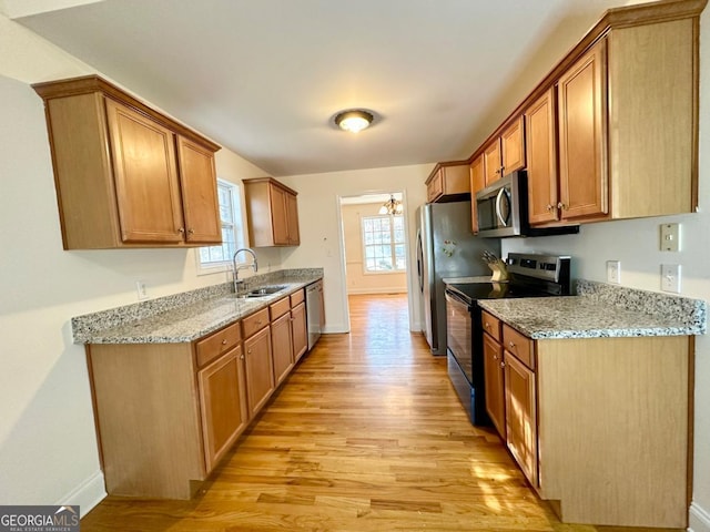 kitchen with sink, an inviting chandelier, appliances with stainless steel finishes, light stone countertops, and light hardwood / wood-style floors