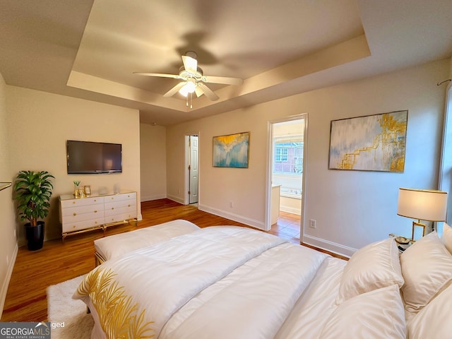 bedroom with a raised ceiling, hardwood / wood-style flooring, connected bathroom, and ceiling fan