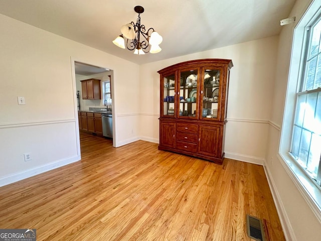 unfurnished dining area with sink, a chandelier, and light hardwood / wood-style floors