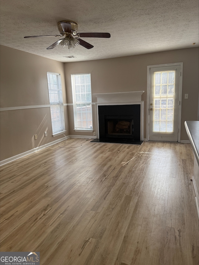 unfurnished living room with ceiling fan, a textured ceiling, and light wood-type flooring