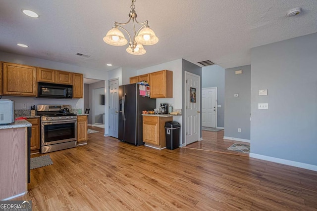 kitchen featuring pendant lighting, wood-type flooring, a textured ceiling, and black appliances