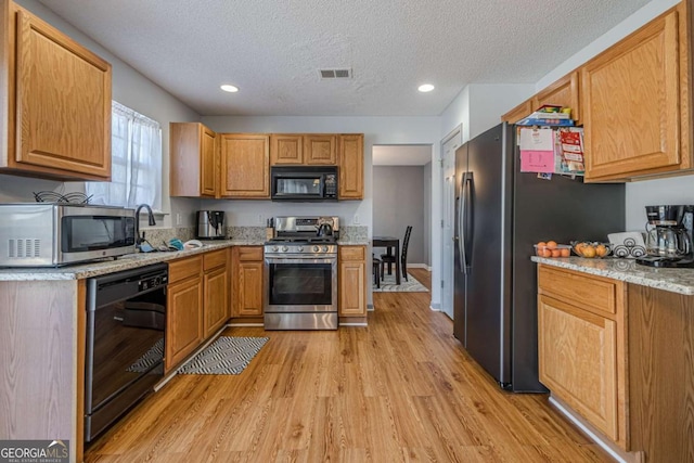 kitchen featuring light stone countertops, black appliances, a textured ceiling, and light wood-type flooring