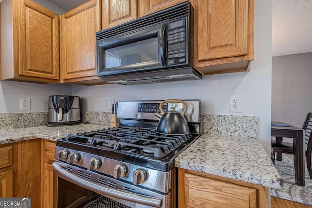 kitchen with gas range, light stone counters, and a textured ceiling