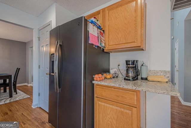 kitchen featuring stainless steel fridge, light brown cabinetry, light hardwood / wood-style floors, and a textured ceiling