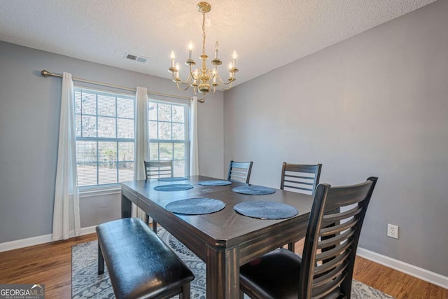 dining area featuring hardwood / wood-style floors, a textured ceiling, and an inviting chandelier