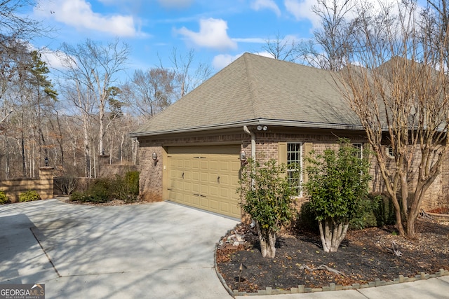 view of property exterior with concrete driveway, brick siding, an attached garage, and roof with shingles
