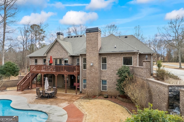 rear view of house with brick siding, a patio, a chimney, a deck, and stairs