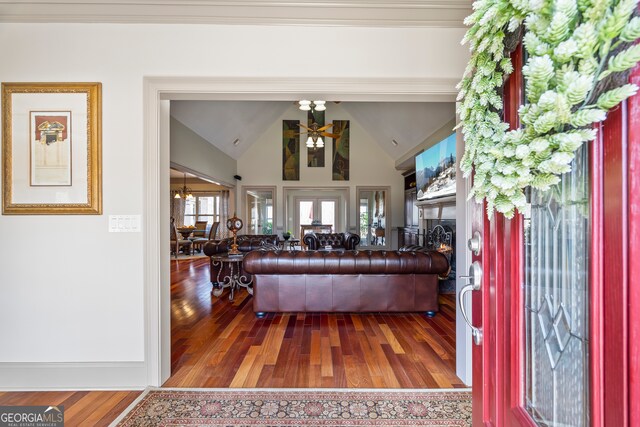 living area with a warm lit fireplace, high vaulted ceiling, wood finished floors, and an inviting chandelier