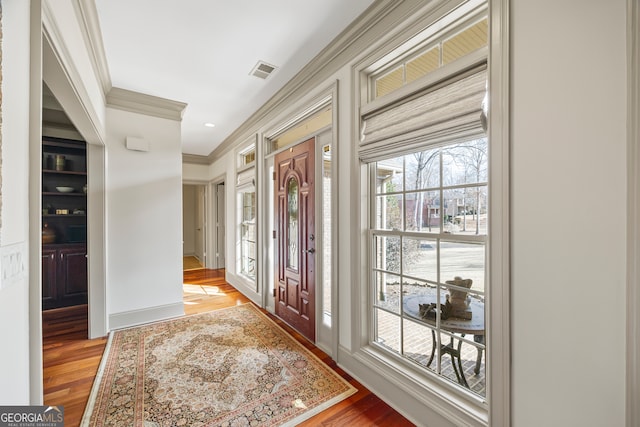 foyer with ornamental molding, visible vents, and wood finished floors