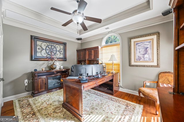 office space with dark wood-type flooring, a tray ceiling, crown molding, and baseboards