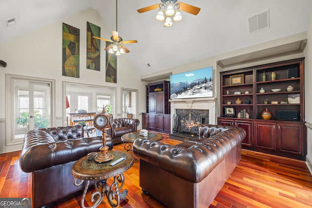 living room featuring hardwood / wood-style flooring, a high end fireplace, high vaulted ceiling, and ceiling fan