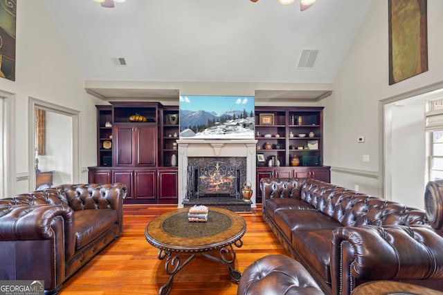 living room featuring high vaulted ceiling, built in shelves, a fireplace, and light hardwood / wood-style floors