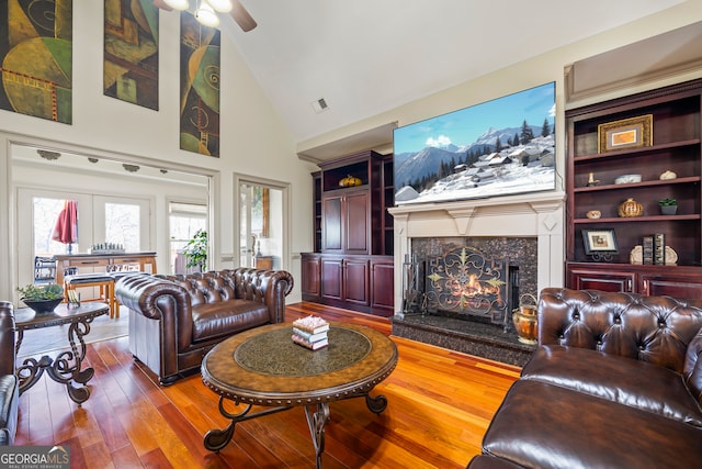 living room with hardwood / wood-style floors, high vaulted ceiling, a fireplace, ceiling fan, and built in shelves