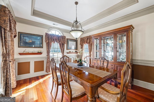 dining room with a wainscoted wall, wood finished floors, visible vents, ornamental molding, and a raised ceiling