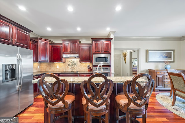 kitchen with light stone counters, appliances with stainless steel finishes, a kitchen island with sink, and a breakfast bar area