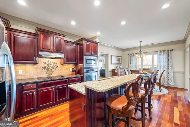 kitchen with dark stone counters, a kitchen island, stainless steel appliances, dark brown cabinets, and under cabinet range hood