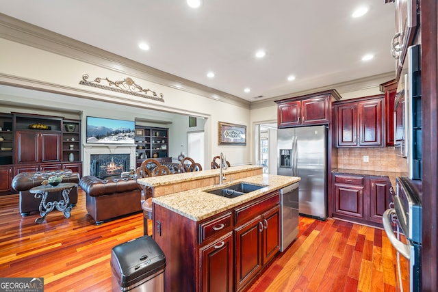 kitchen with sink, hardwood / wood-style floors, stainless steel appliances, ornamental molding, and an island with sink