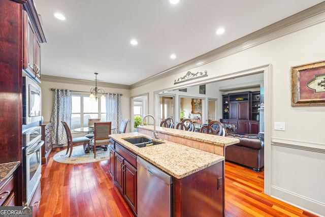 kitchen featuring sink, crown molding, hanging light fixtures, appliances with stainless steel finishes, and a kitchen island with sink