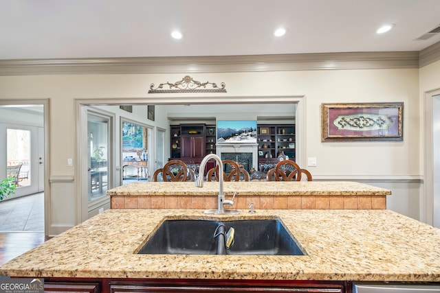 kitchen featuring sink, crown molding, an island with sink, light stone countertops, and hardwood / wood-style floors