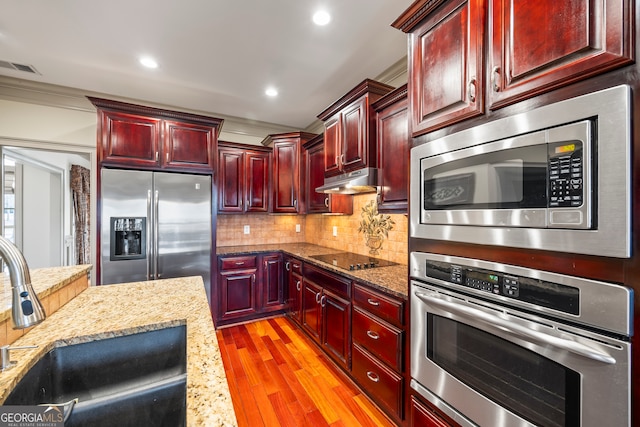 kitchen with sink, light stone counters, light hardwood / wood-style flooring, appliances with stainless steel finishes, and decorative backsplash