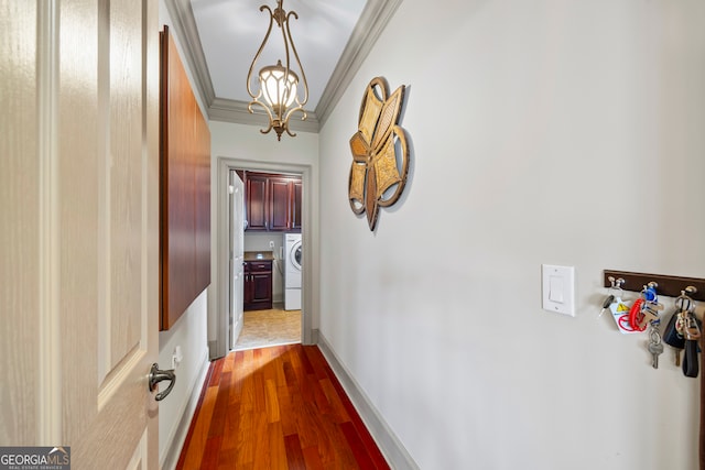 hallway with washer / dryer, baseboards, dark wood-style flooring, crown molding, and a notable chandelier