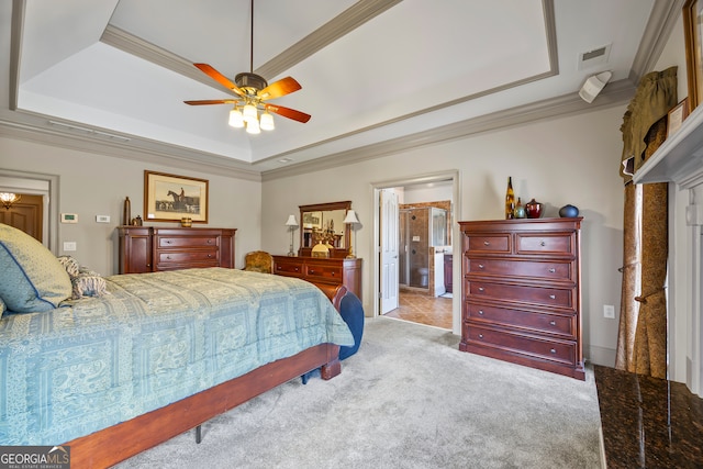 bedroom with light carpet, ensuite bath, a tray ceiling, and ornamental molding