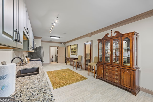 kitchen featuring baseboards, stainless steel microwave, ornamental molding, light stone countertops, and a sink