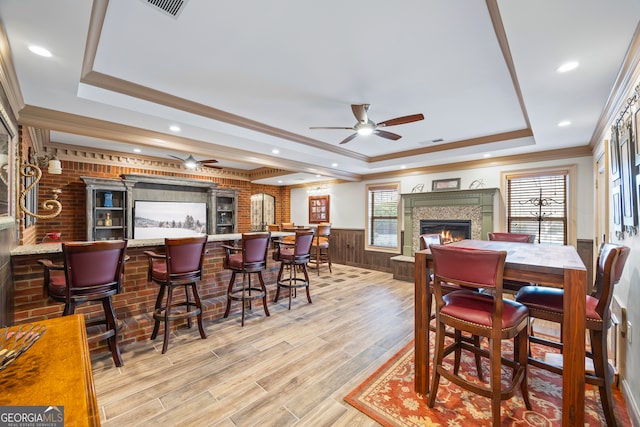 dining room featuring crown molding, light hardwood / wood-style flooring, ceiling fan, bar, and a raised ceiling