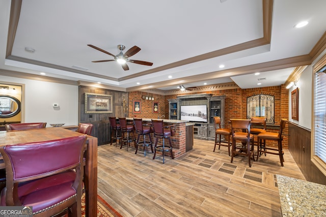 dining space with a raised ceiling, crown molding, brick wall, and bar