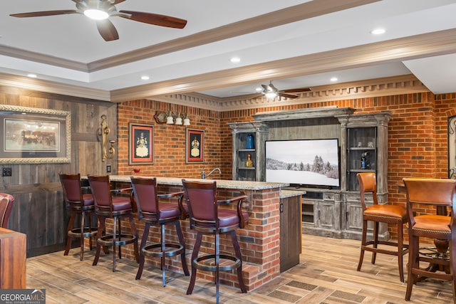 bar with crown molding, ceiling fan, brick wall, and light hardwood / wood-style flooring