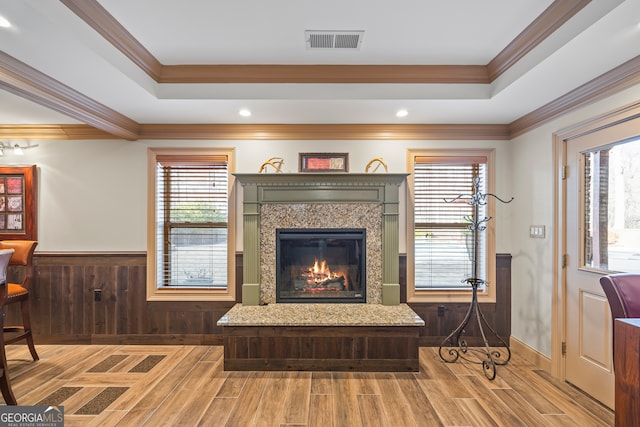 living area with light wood finished floors, visible vents, wainscoting, a glass covered fireplace, and a tray ceiling