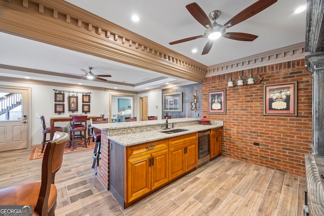 kitchen with light stone counters, wine cooler, brown cabinetry, wood tiled floor, and a sink