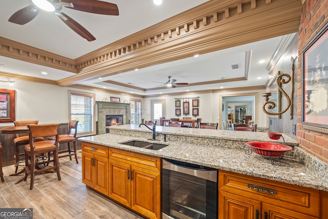 kitchen with sink, light stone counters, a tray ceiling, beverage cooler, and light wood-type flooring