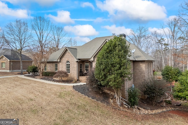 view of front of house featuring roof with shingles, brick siding, a chimney, and a front yard