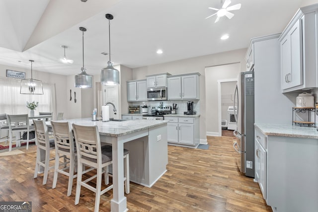 kitchen featuring light stone countertops, light wood-style flooring, stainless steel appliances, and backsplash