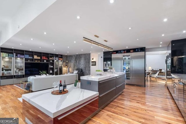 kitchen with built in refrigerator, a large island, light stone countertops, and light hardwood / wood-style floors