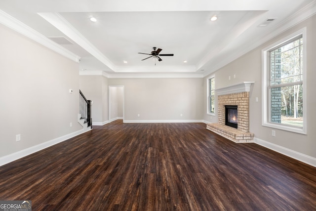 unfurnished living room with ornamental molding, dark hardwood / wood-style floors, a fireplace, and a tray ceiling