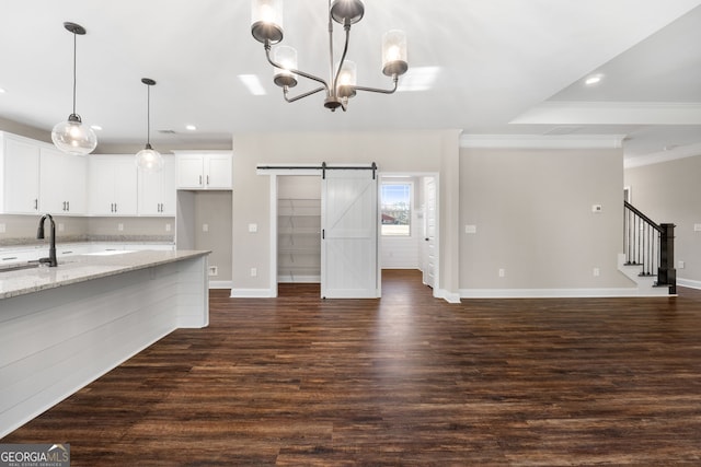 kitchen with dark wood-type flooring, light stone counters, ornamental molding, a barn door, and white cabinets