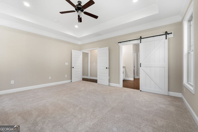 unfurnished bedroom featuring crown molding, light colored carpet, a barn door, and a raised ceiling