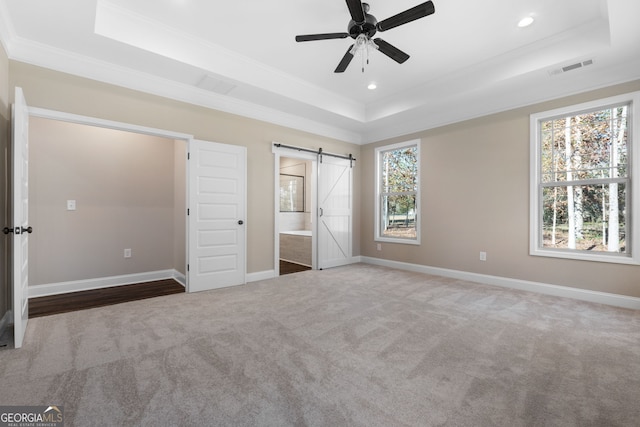 unfurnished bedroom featuring crown molding, ensuite bath, carpet, a tray ceiling, and a barn door