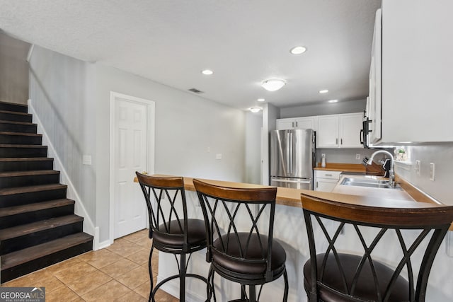 kitchen with sink, light tile patterned floors, a breakfast bar, appliances with stainless steel finishes, and white cabinetry