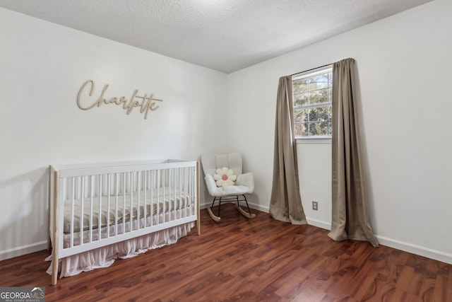 bedroom featuring dark hardwood / wood-style flooring, a textured ceiling, and a crib