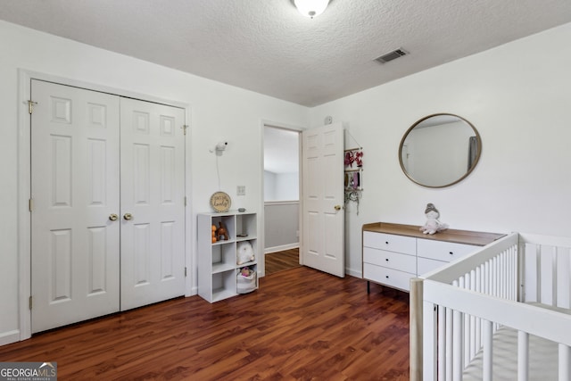 bedroom with a crib, dark wood-type flooring, a textured ceiling, and a closet