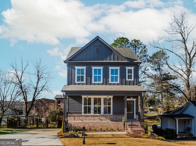 view of front facade with covered porch, board and batten siding, a front yard, a shingled roof, and brick siding