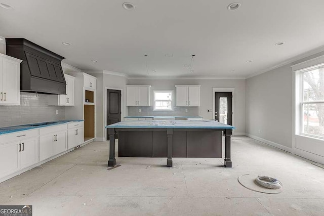 kitchen featuring a kitchen island, white cabinetry, crown molding, cooktop, and baseboards