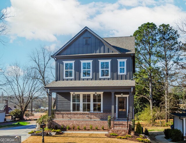 view of front facade with covered porch, board and batten siding, and roof with shingles