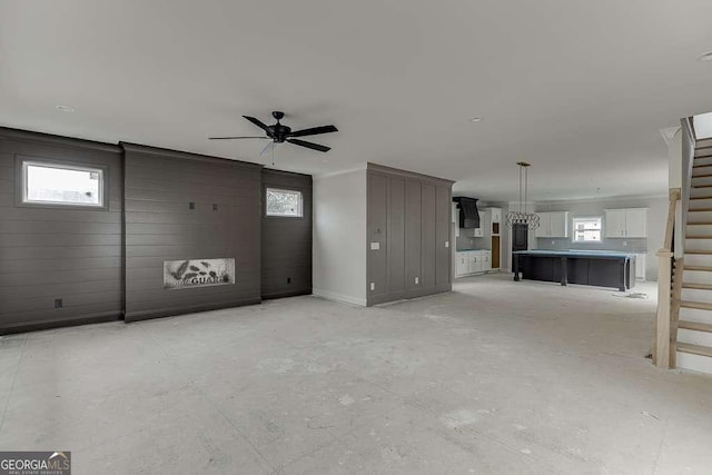 unfurnished living room featuring baseboards, a ceiling fan, and stairs