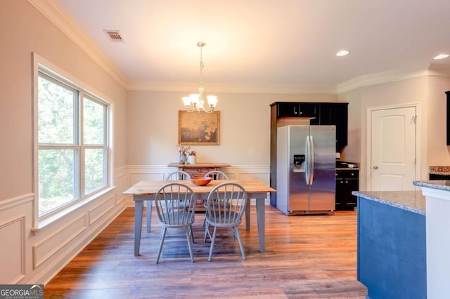 dining area with hardwood / wood-style flooring, crown molding, and an inviting chandelier