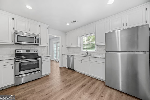 kitchen featuring white cabinetry, sink, stainless steel appliances, light stone countertops, and light wood-type flooring